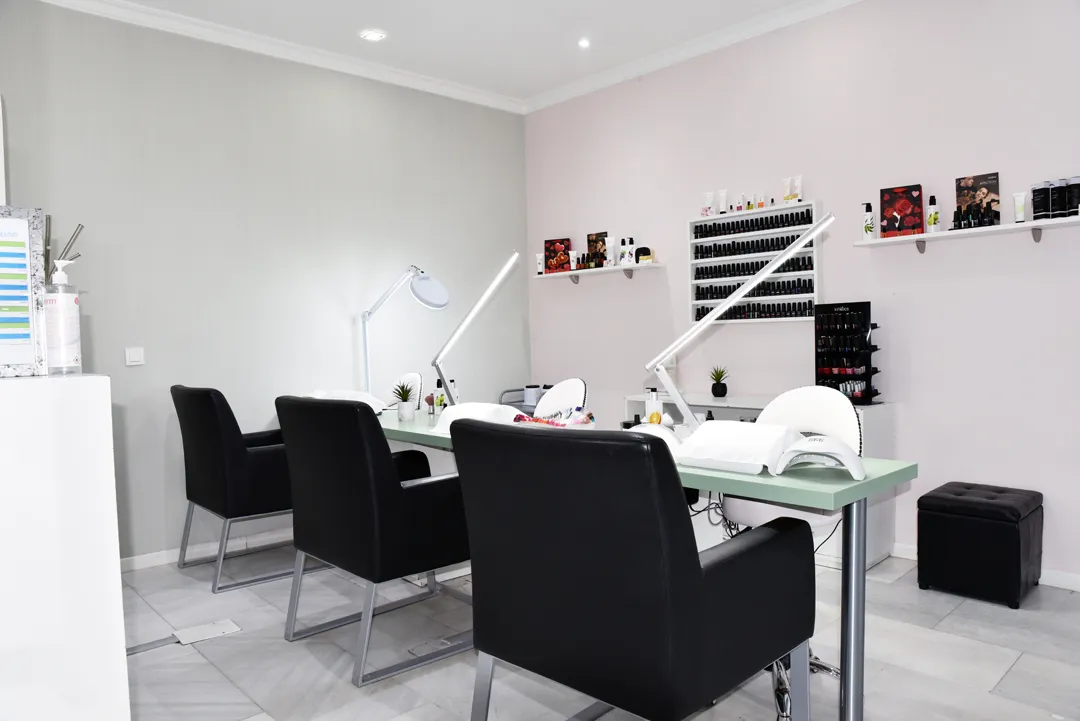 Interior del salón: tres puestos de manicura con sillones negros, lámparas de luz fría y el expositor de esmaltes al fondo